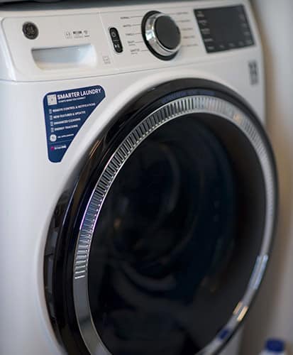 Close-up of a modern front-loading washing machine with a digital control panel and a label that reads "Smarter Laundry" on the upper left side of the door.