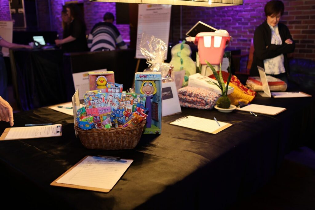 Silent auction table with donated gift baskets and bid sheets at the Outreach on 7th Euchre Party