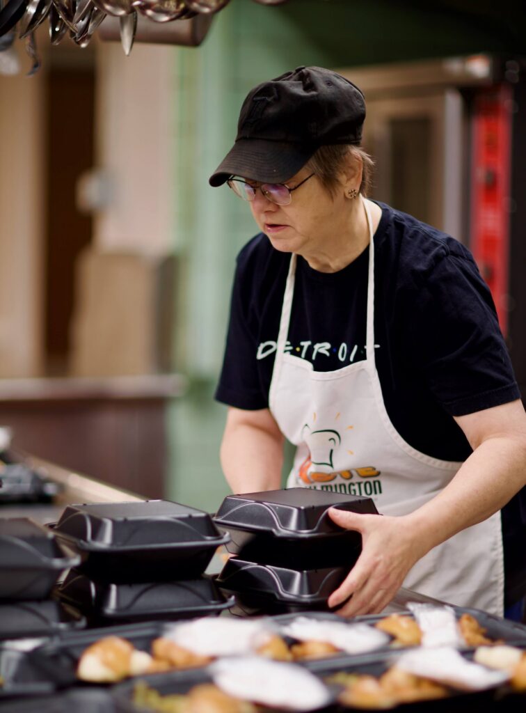 A volunteer in an apron packing take-out lunches in the church kitchen at Outreach on 7th